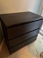 Front view of black brown IKEA dresser showing three drawers and wood grain texture.