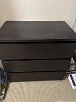 Front view of black 3-drawer IKEA MALM dresser standing against wall on carpeted floor.