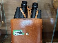 Brown leather carrying case containing black Fisher-Dietz binoculars with textured grip and strap.