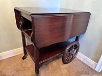 Folded tea wagon table showing side profile with large spoked wheels and caster wheels.