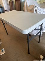 Side angle showing white textured foldable tabletop and black metal legs.