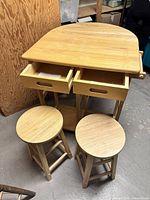 Wooden folding bar table with two open drawers and three stools in front of the table.