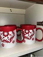 Two white ceramic coffee mugs with red interior and festive red design.