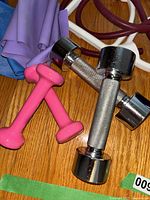 Photo showing two metal dumbbells with knurled grips and two small pink vinyl dumbbells on a wooden floor.
