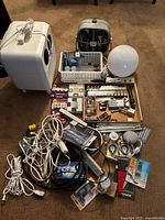 Lot overview showing Bella heater, small fan, Google Home Mini, basket with batteries and hardware, multiple cables and light bulbs.