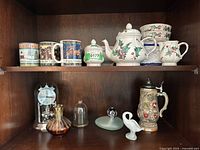 Image showing the porcelain tea set with holly pattern on top shelf, mugs, decorative clock with clear dome, amber colored vase, swan figurine, and vintage beer stein on the second shelf