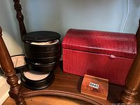 Photo showing the large red faux crocodile skin jewelry case, the multi-tiered round black jewelry box, and the small wooden box together on a wooden shelf.