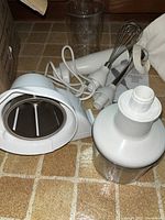 Photo showing KitchenAid immersion blender with whisk and chopping bowl attachments, tall blending cup, and power cord.