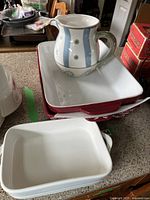 Photo showing three white ceramic baking dishes stacked and the decorative jug placed on top; jug has blue vertical stripes and flower motifs.