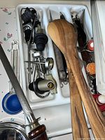 Drawer of various kitchen utensils and bar tools including wooden spoons, corkscrews, bottle stoppers, and sharpening steel.