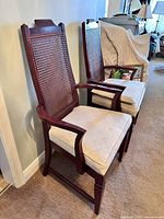 Two mid-century modern dining chairs with woven cane backs and upholstered seats, showing wood frames and armrests on the end chair.