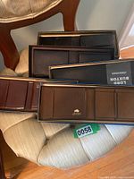Five men's leather wallets on a chair in their original Lord Buxton boxes showing packaging and color variety including brown and black leather