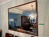 Full view of the rectangular mirror with wood frame mounted on a wall reflecting a chandelier and furniture.