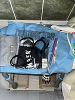 Photo showing blue hot water bottle with cover, electric heating pad, handheld back scratcher, and straps on blue cloth surface with gray/pink legs visible