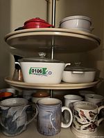 View of mugs below Pyrex baking dishes on lazy susan, showing bird-themed ceramic mugs including 'British Birds' and others with herons and floral designs.