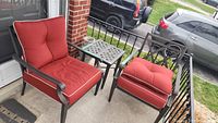 Two metal patio chairs with red cushions and matching metal side table arranged on porch