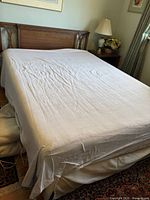 Full view of bed with white fitted sheet covering mattress area revealing wooden frame and box spring.