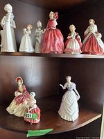 Two-shelf wooden cabinet displaying multiple porcelain figurines.