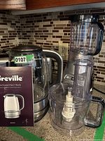 Breville kettle with user manual and blender parts on kitchen counter against tiled backsplash.