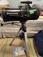 Full side view of the Celestron PowerSeeker 127EQ telescope mounted on aluminum tripod with instruction manuals laid on floor beneath tripod.