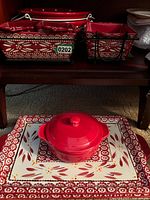 Set of red kitchenware items arranged on shelf including casserole, baking trays, and condiment bowls with matching patterns