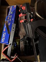 Overall view of various hand tools including saws, clamps, and boxed tool set, stored together in a toolbox or container.