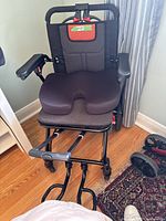 Front view of the transport chair showing padded seat with contour cushion and armrests on wooden floor.