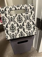 Photo showing a patterned white and black fabric storage bin with a cutout handle and a purple fabric storage bin beneath it.