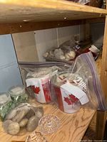 Various bags of craft stones and small jars containing stones or craft materials placed on a wooden surface.