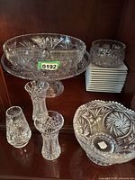 Wide view of vintage crystal displaying a large pedestal bowl, medium round bowl, a stack of small plates with small bowl on top, and three small vases in front.