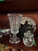 Full view of crystal vase, glass bowl, lidded jar, and pitcher on wooden shelf
