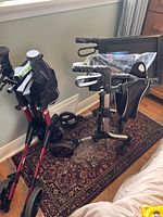 Two foldable rollators side by side, one red with three wheels, one silver with four wheels and tray attached