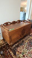 Full side view of the wooden cedar chest showing carved detailing on the top edge and front panel with carved legs.