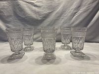 Six clear Cape Cod style glasses evenly spaced on a surface, showing overall set condition and shape.