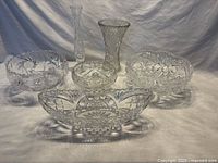 Front view of six cut glass pieces including footed bowls and vases arranged on a white background.