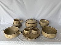 Full view of the entire Denby Memories set showing multiple types of bowls and plates arranged on fabric background.