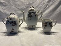 Full view of the Limoge coffee/teapot, sugar bowl with lid, and creamer, all white porcelain with brown floral and gold trim.
