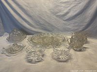 Full set of mixed cut and pressed glass items including creamer, sugar bowl, juicer, covered butter dish, footed bowls, and server platter arranged on a cloth backdrop.