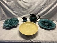 Front view of all five items displayed: large yellow bowl, two green pitchers, and two blue-green dishes including floral and swirl designs.