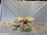 Full view of lot items on white cloth backdrop showing various ceramic and glass serving dishes, creamers, sugar bowls, plates, and bowls.