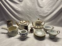 Full lot arrangement showing teapots, Noritake set, vases, and sauce boat on white cloth.