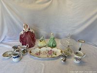 Wide view of all items: figurines, creamers, mug, plate, compote, and vase displayed on cloth background.