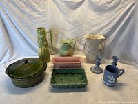 Full lot of nine ceramic and pottery items arranged on white fabric backdrop showing all different shapes, sizes, and colors.