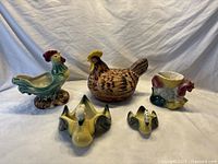 Full view of all ceramic poultry items arranged on cloth background showing rooster, chicken, multiple ducks.