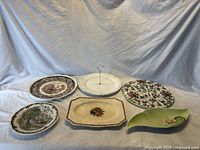 Six ceramic plates and serving pieces arranged on a white surface with light background.