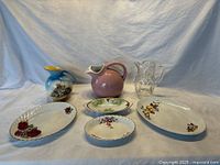 All six items of the lot arranged on white cloth with blue backdrop showing serving platters, celery dishes, and pitchers.