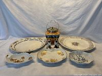 Wide view displaying all seven ceramic and porcelain pieces including platters, biscuit barrel, condiment set, and shakers