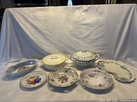 Overview of seven assorted porcelain serving and decorative dishes on white cloth background.