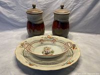 Full view of all items: two Laurentien pottery jars with lids behind, on top of oval perforated floral serving dish, placed on Grindley 16-inch Cream Petal serving platter