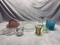 Full lot overview showing various glassware items including clear, blue, green, and pink glass pieces with distinctive patterns.